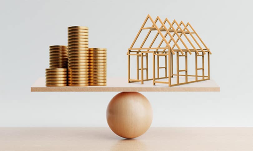 a graphic balancing coins against a small framed house under construction to show the importance of budgeting.