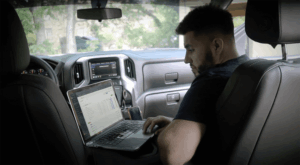 A builder sits in his work truck while working on a laptop