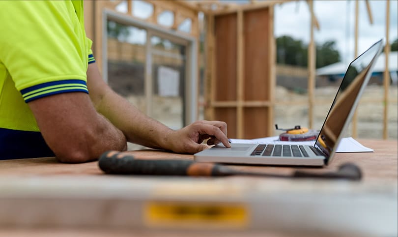 A builder on a construction site using a laptop