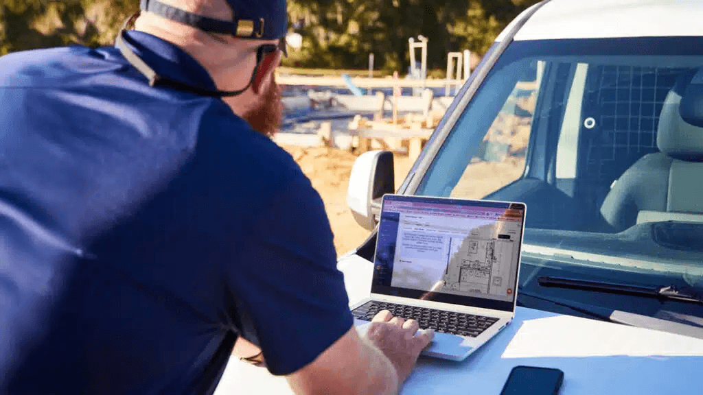 Residential builder reviewing construction drawings on a laptop while preparing a construction takeoff at a job site