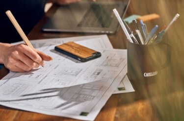 A person working on a set of plans with a pencil on a desk