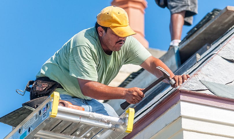 A builder hammering a nail into a roof