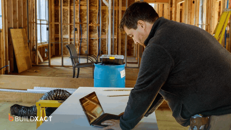 A residential general contractor reviews a job estimate on a tablet at a job-site table with house plans nearby.