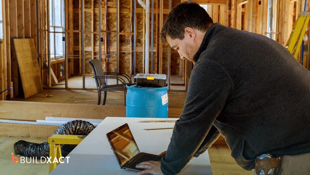 A residential general contractor reviews a job estimate on a tablet at a job-site table with house plans nearby.